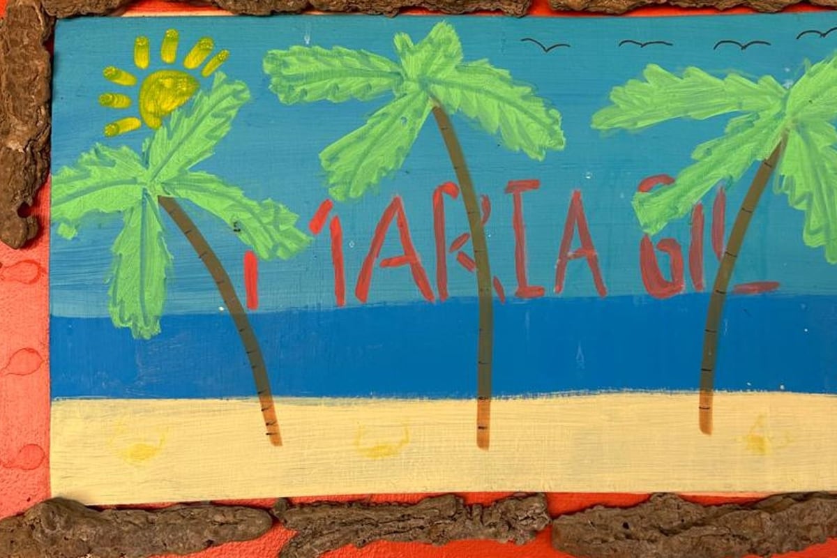 A beach scene with palm trees and the name 'Maria G.' painted on a wooden board.