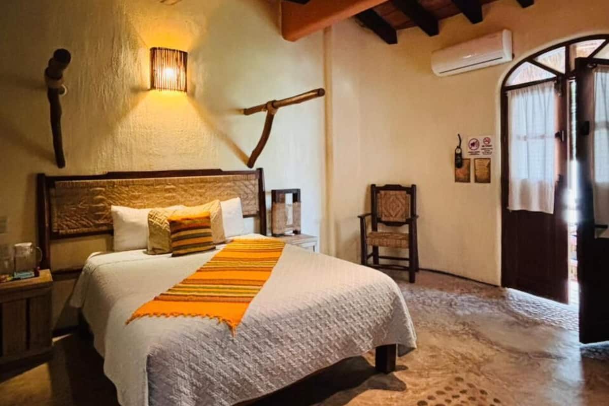 A bedroom with a bed, a wall-mounted lamp, a chair, and a wooden ceiling.