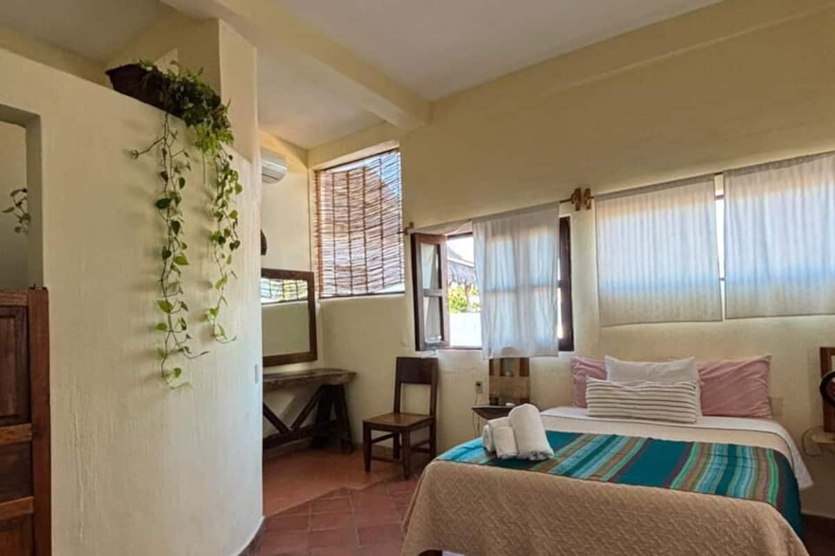 A bedroom with a bed, a desk, a chair, and a window with blinds.