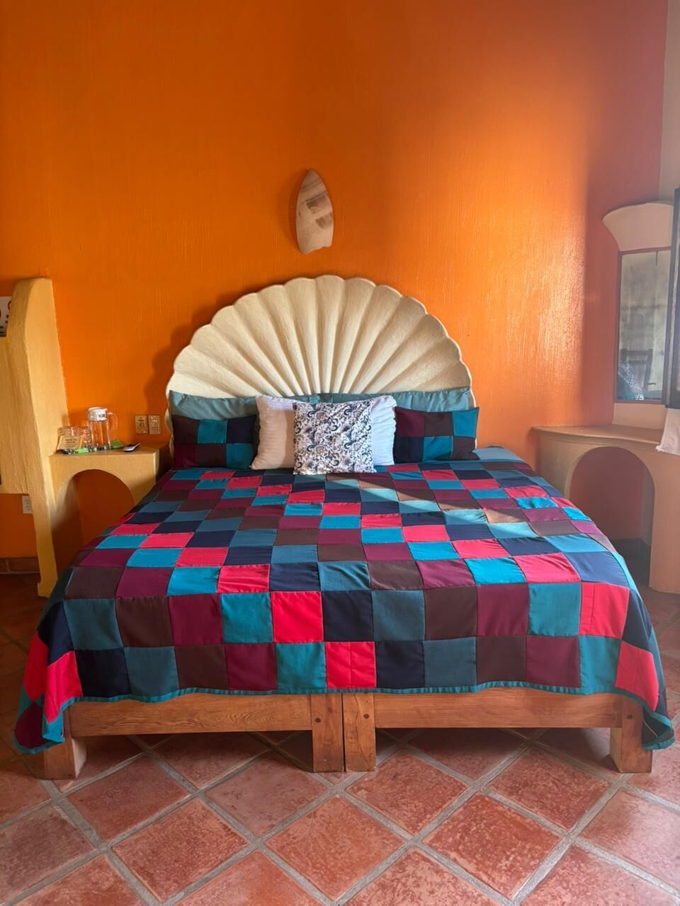 Una cama con colcha de cuadros, cabecera de madera y suelo de baldosas.