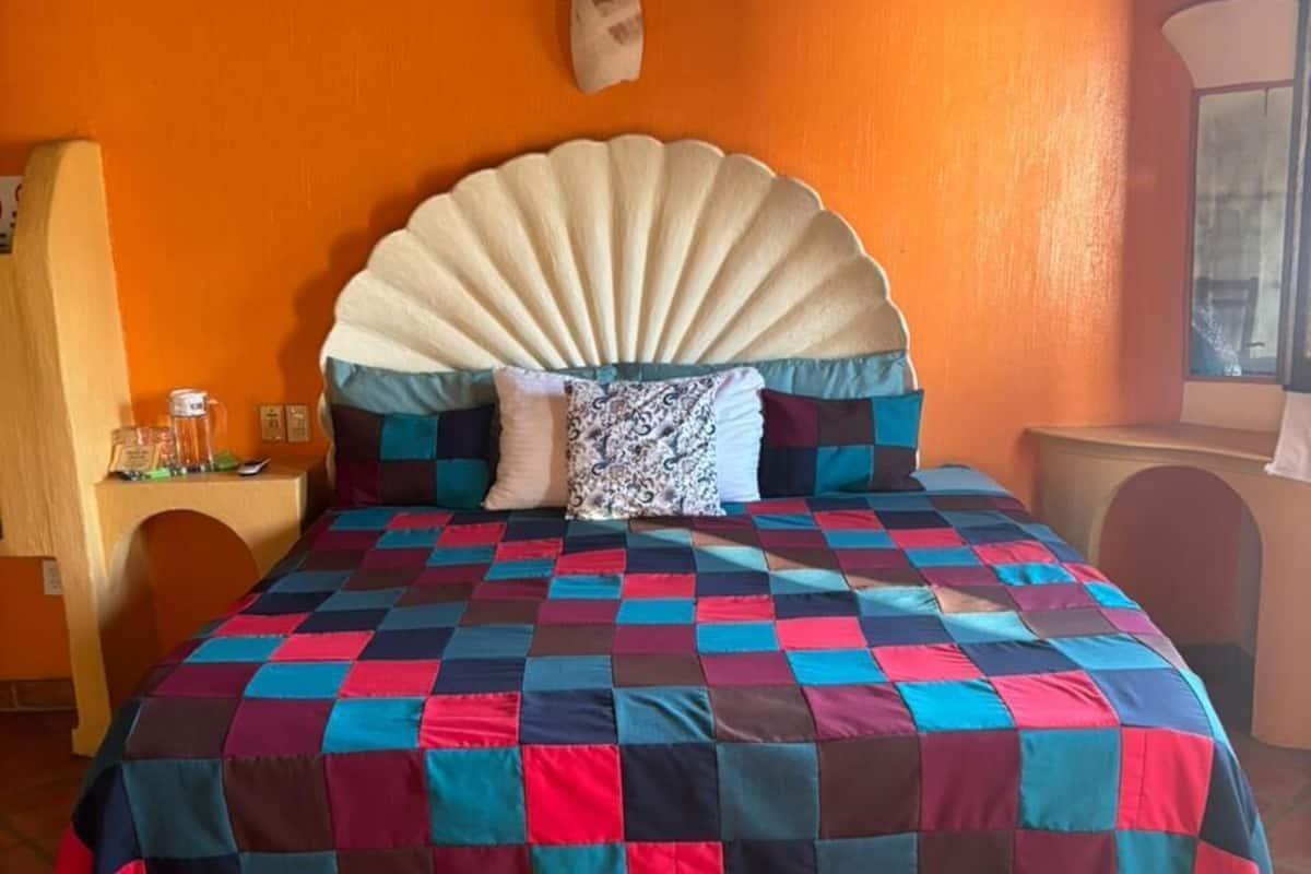 A bed with a checkered quilt, a wooden headboard, and a tiled floor.