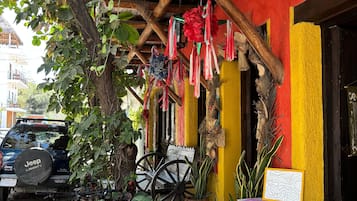 Placa de madeira do Hotel Palomera Artesanal, uma bicicleta, plantas em vasos e um carrinho de mão na área externa.