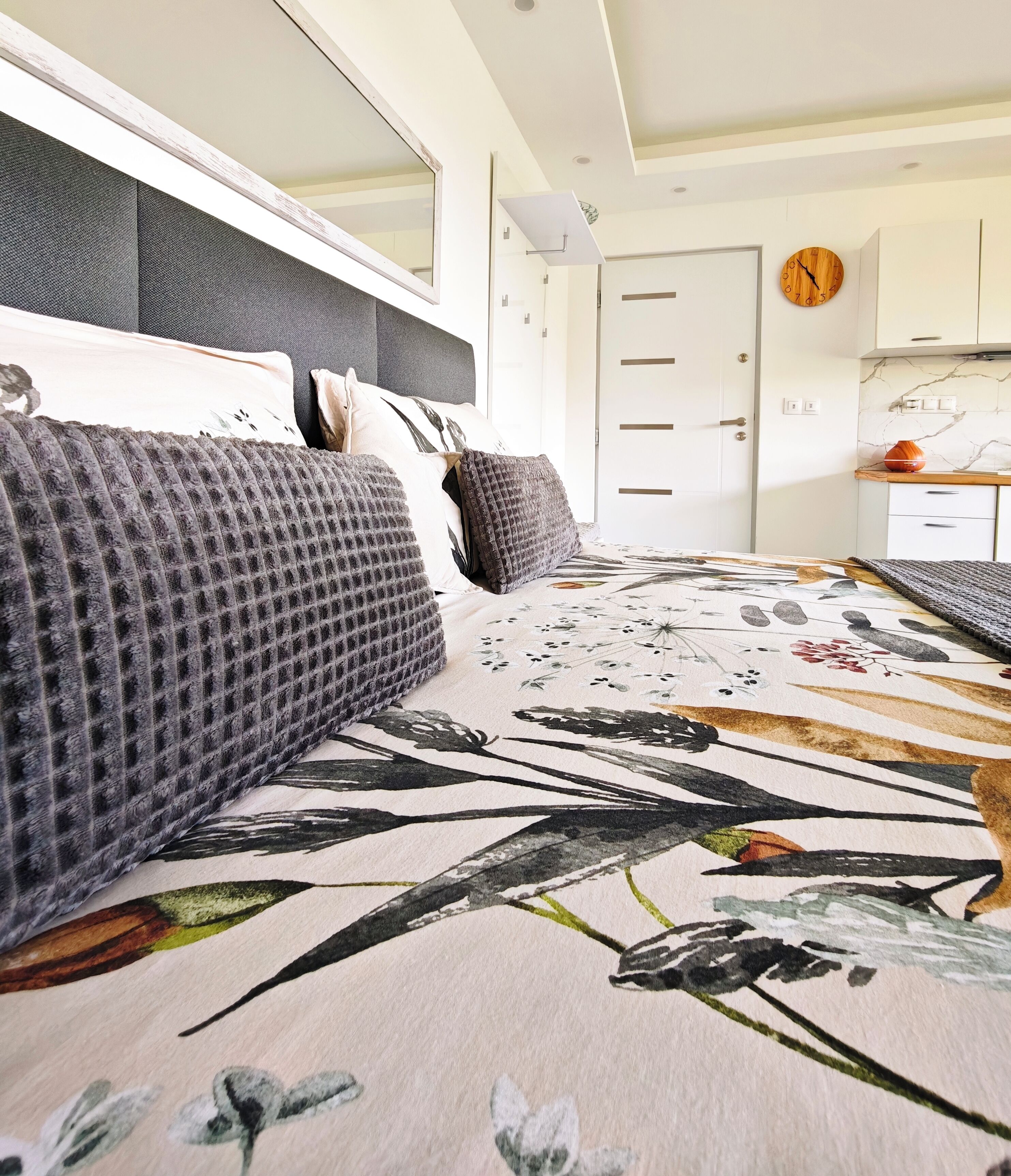 Une chambre à coucher avec un lit, une commode, un miroir, une horloge et une porte.