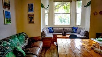 A cozy living room with a wooden table, a sofa, and a window with a view of greenery.