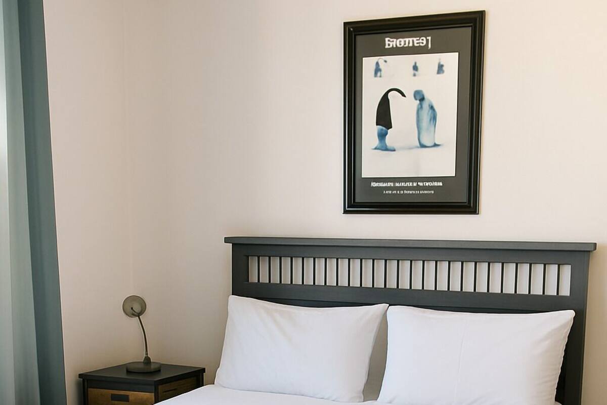 Una cama bien hecha con ropa de cama blanca y azul, un cabecero oscuro y un cuadro en la pared.
