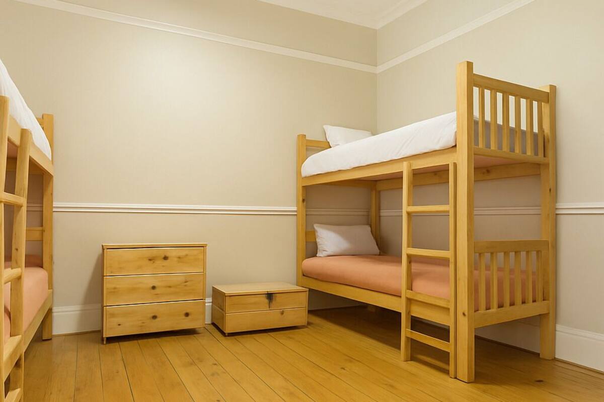Habitación con literas, piso de madera, una cómoda pequeña de madera y una mesita de noche.