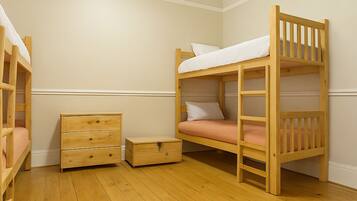 Une chambre avec un lit superposé, un plancher en bois, une petite commode en bois et une table de chevet.