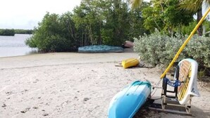 Una playa arenosa con un kayak azul y un bote amarillo.