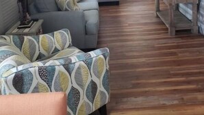 Un espacio habitable compacto con un sofá, un sillón estampado, una mesa de centro de madera y un televisor.