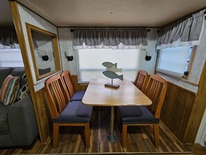 Un intérieur de camping-car compact comprenant une table à manger, quatre chaises en bois, un banc rembourré et une sculpture décorative représentant un poisson.