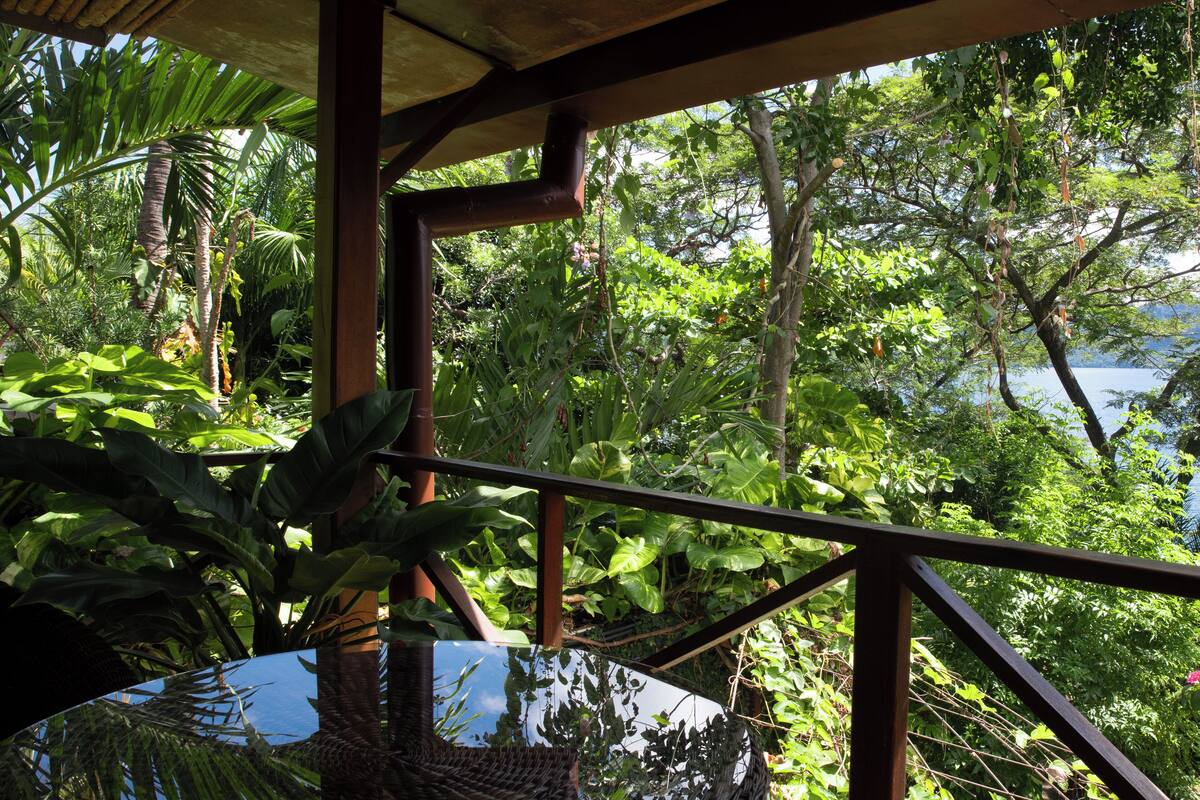 A hammock under a wooden structure with a view of lush greenery and a body of water.