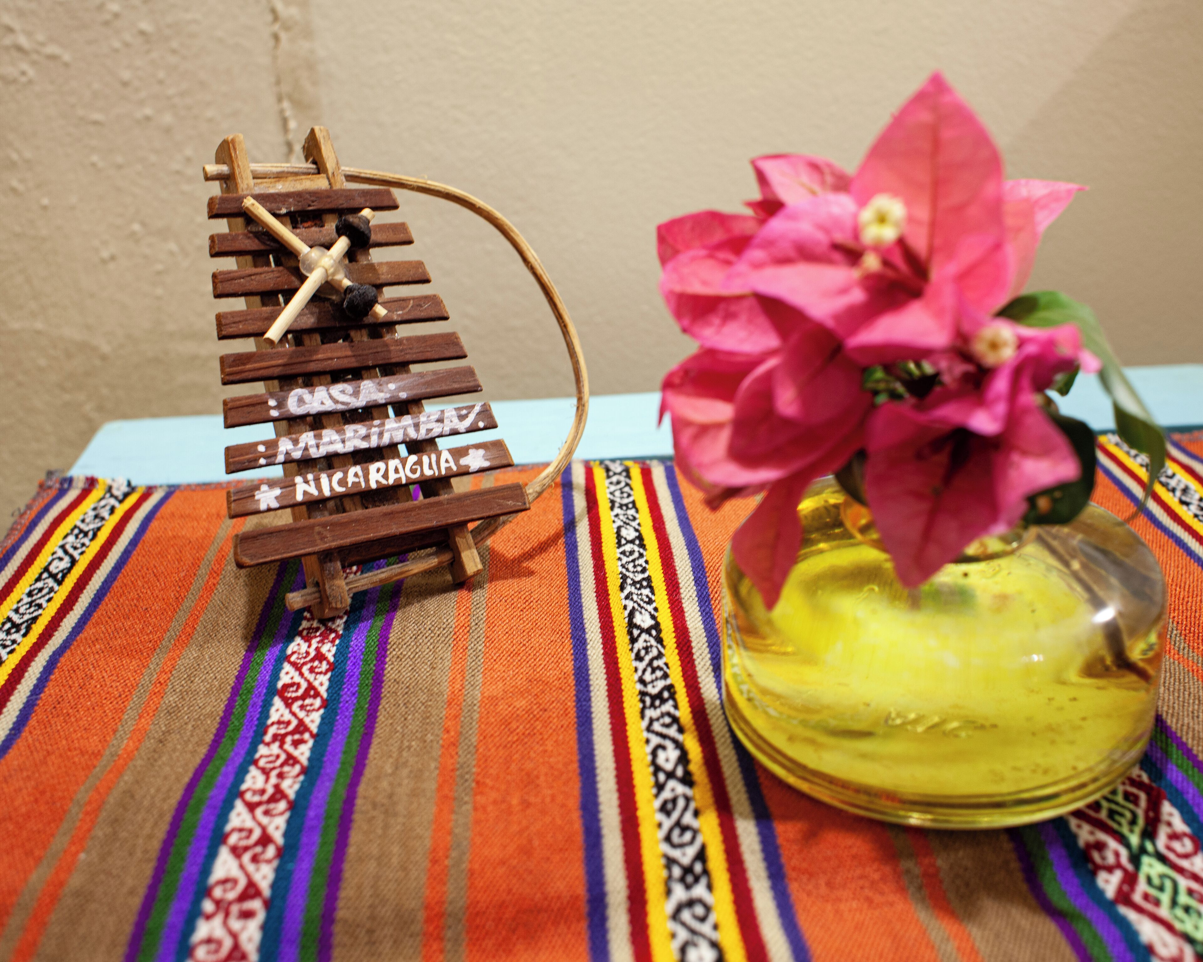 A wooden sign with names, a pink flower in a glass vase, and a striped fabric.