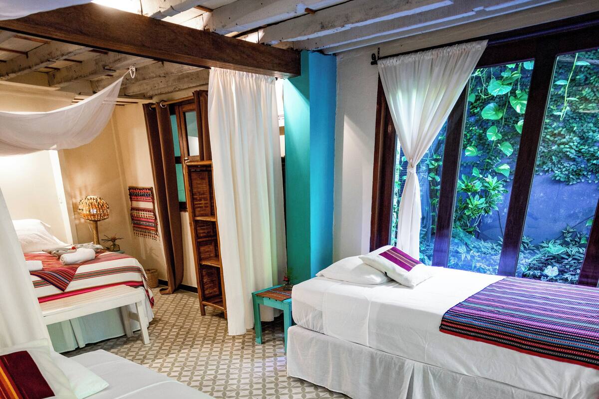 A room with two beds, a small table, and a window with curtains.