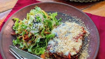 A plate with a piece of lasagna and a side salad on a wooden table.