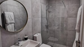 Une salle de bain moderne avec un grand miroir rond, un lavabo, des toilettes et un espace douche.