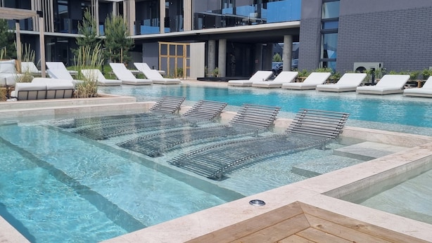 Un espace piscine moderne avec une eau cristalline, des chaises longues et un bâtiment doté de grandes fenêtres en arrière-plan.