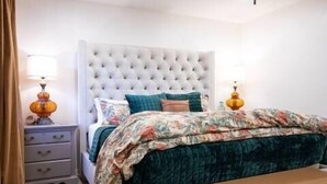 A bedroom with a tufted headboard, floral bedding, bedside lamps, and a bench. - The Eden, 1BR Queen Duplex by Velvet Ditch Villas (Oxford)