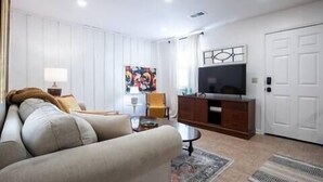 A living room with a sofa, a TV, a cabinet, and a painting on the wall. - The Eden, 1BR Queen Duplex by Velvet Ditch Villas (Oxford)