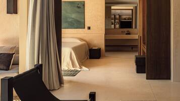 Una habitación de hotel moderna con una cama, una zona de estar con una silla, un espejo grande y un baño con lavamanos y espejo.