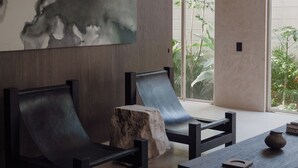 Um interior moderno com uma grande pintura abstrata, duas cadeiras pretas, uma mesa de madeira e um tronco de pedra.