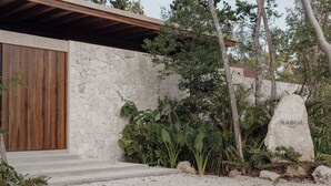Um edifício moderno com fachada de pedra, porta de madeira e placa de pedra com a inscrição "NABOA".