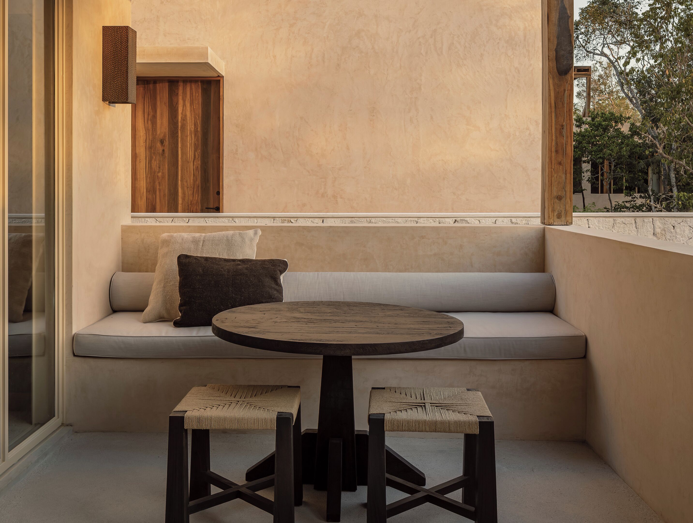A cozy seating area with a round table and two stools, a cushioned bench with pillows, and a wooden wall panel.