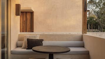 A cozy seating area with a round table and two stools, a cushioned bench with pillows, and a wooden wall panel.