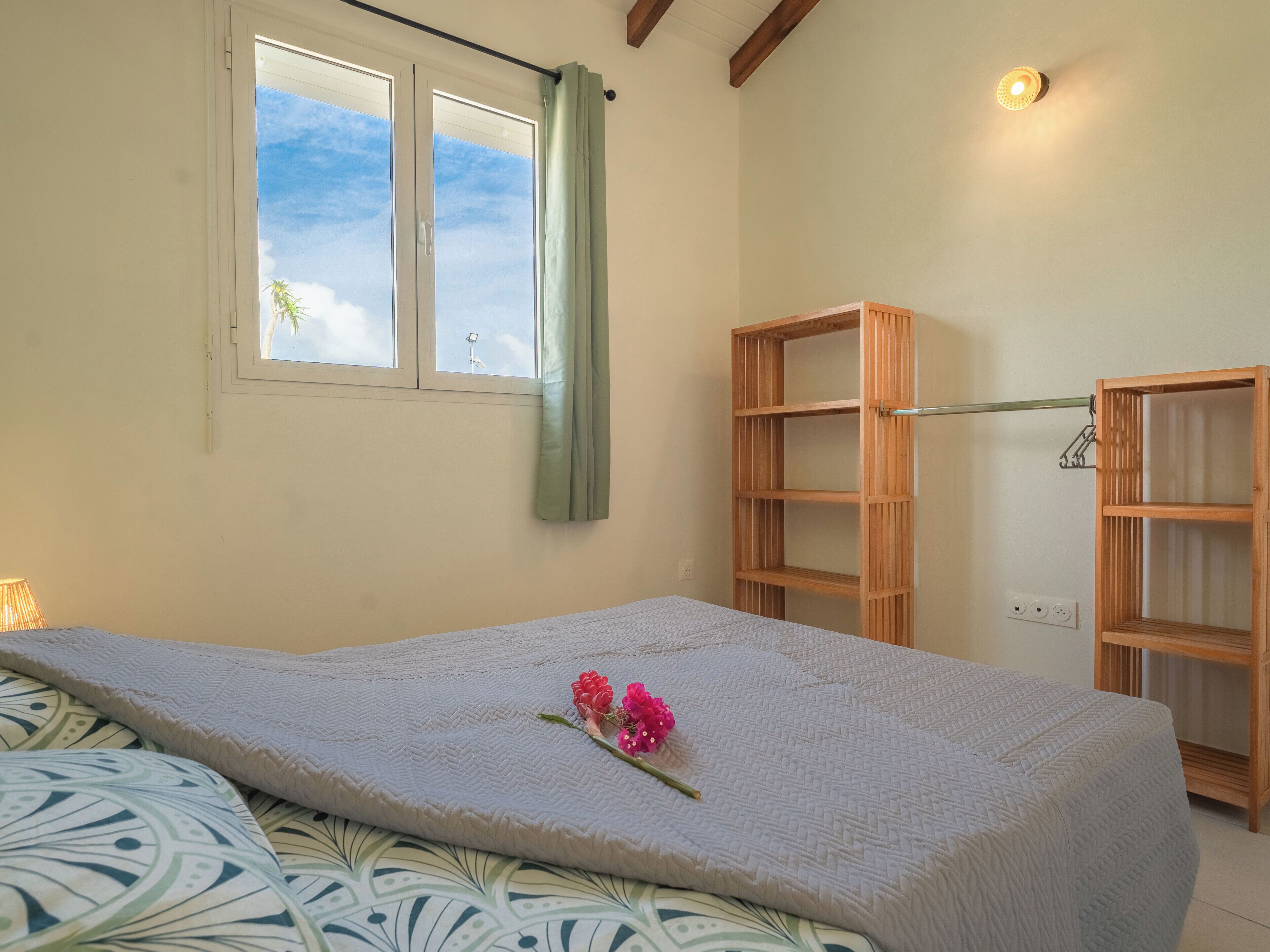Ein Schlafzimmer mit einem Bett, einem Fenster mit Vorhängen, einem Holzschrank und einer Nachttischlampe.