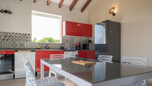 A modern kitchen with red cabinets, a glass table, and white chairs.