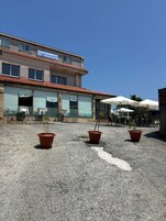 Un edificio con un letrero que dice "RESTAURANT O'PEQUE". Hay mesas y sillas al aire libre, y macetas con plantas en el suelo.