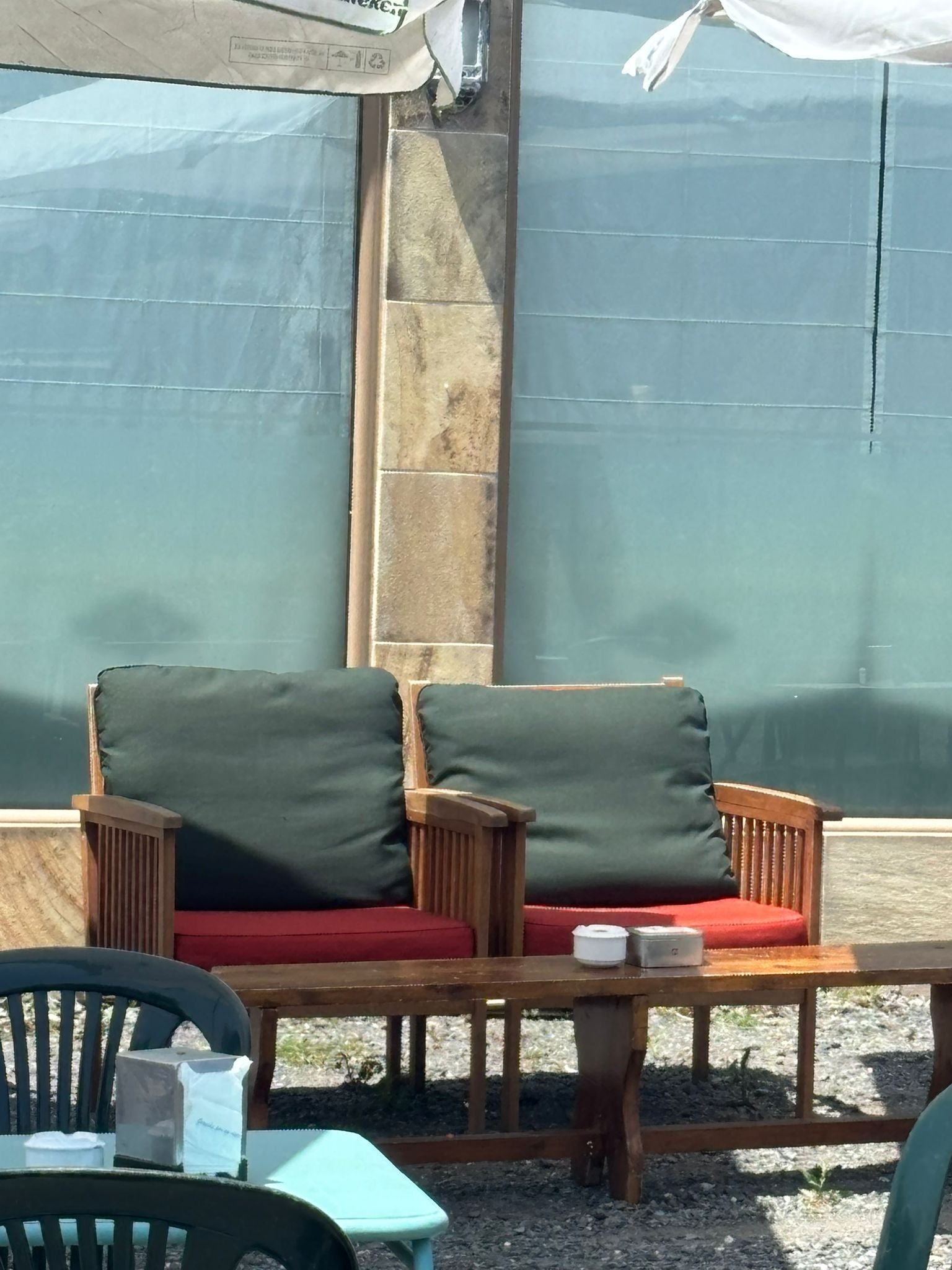 A seating area with two wooden chairs with red cushions, a small table, and a green plastic stool.