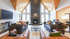 A spacious living room with a stone fireplace, leather sofas, and a large TV mounted on the wall.