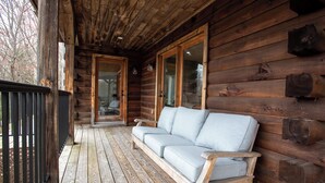 A wooden cabin with a porch, a sofa, and glass doors leading to a room.
