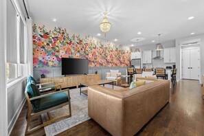 A modern living room with a large sofa, a TV, and a floral wall mural.