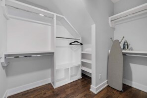Un dressing accessible sans porte, doté d’étagères ouvertes, d’une tringle et d’un espace intégré pour repasser.