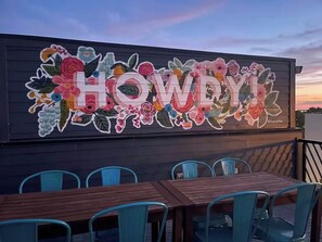 A restaurant with a colorful floral mural on the wall and outdoor seating with blue chairs.