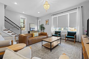 Un salon moderne avec un escalier, un canapé en cuir, une table basse et un lustre.