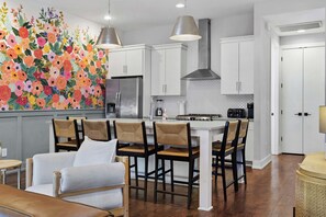 A modern kitchen with white cabinetry, a central island with bar stools, and a colorful floral mural on the wall.