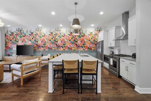 A modern kitchen with a central island, wooden flooring, and a colorful floral wall mural.