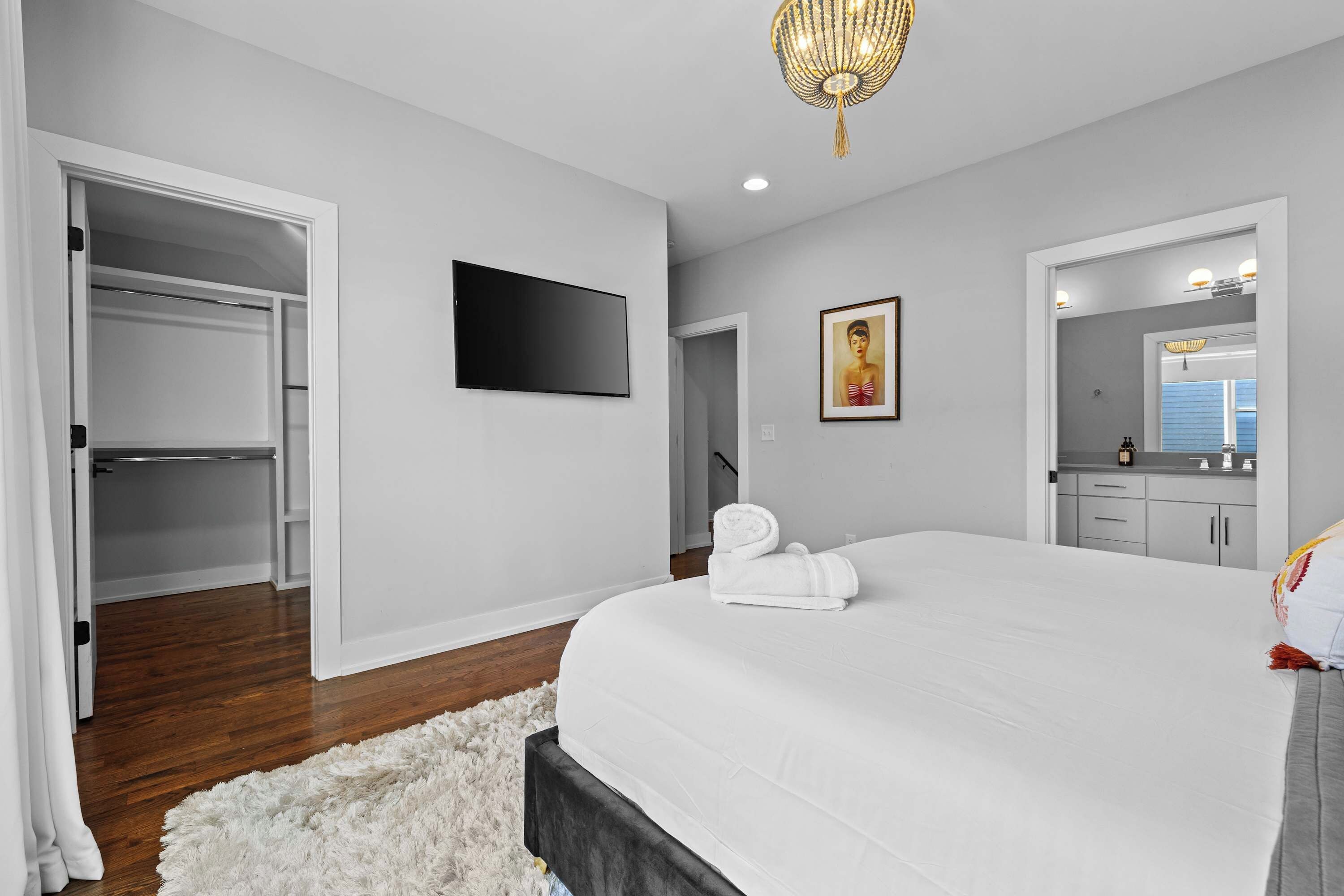 A bedroom with a bed, a TV, a painting, a mirror, and a walk-in closet.