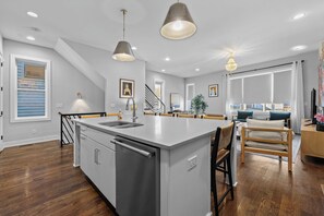Une cuisine moderne dotée d’un îlot central, d’appareils électroménagers en acier inoxydable et de luminaires suspendus.