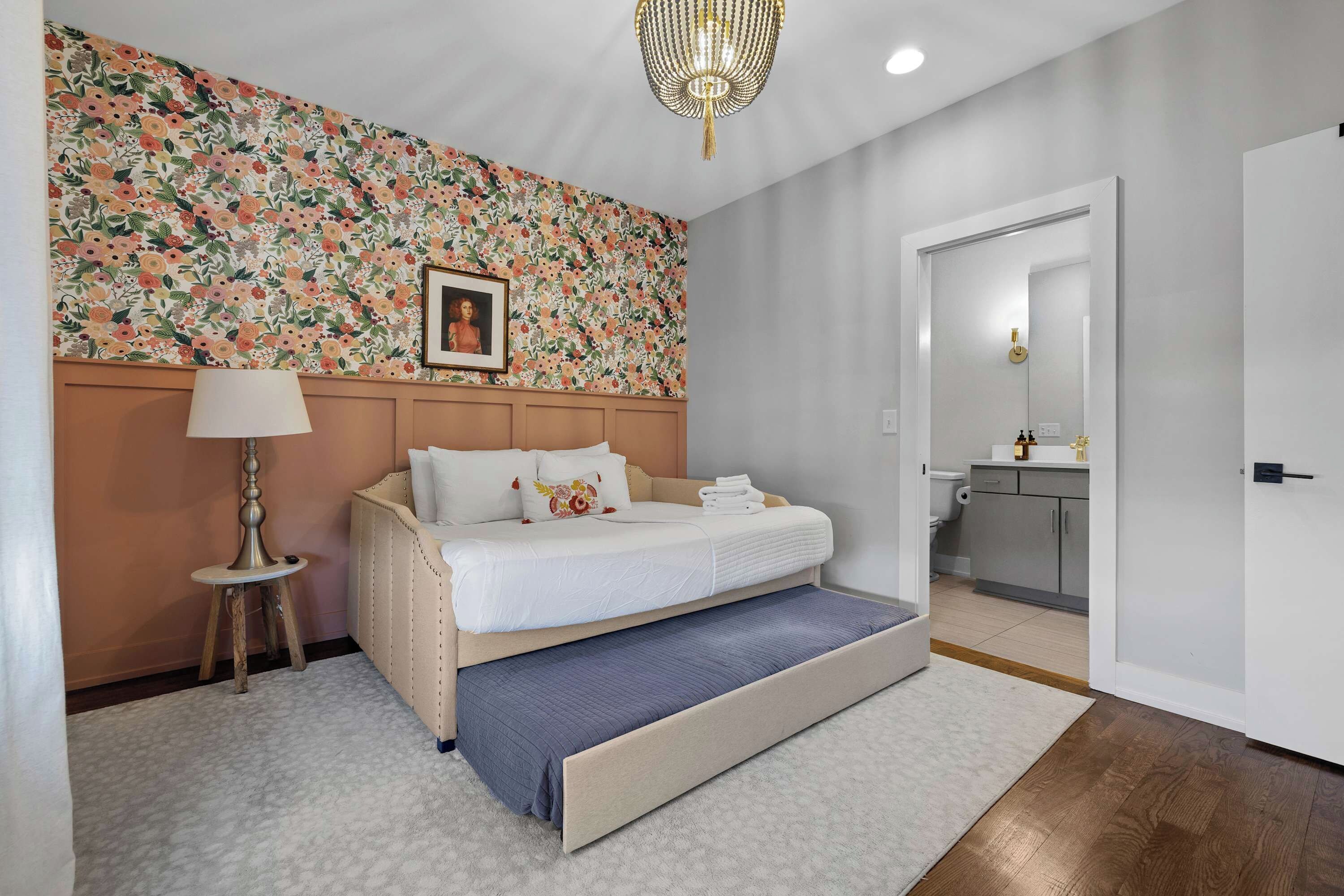 Un dormitorio con cama, mesita de noche, lámpara y un papel tapiz floral.