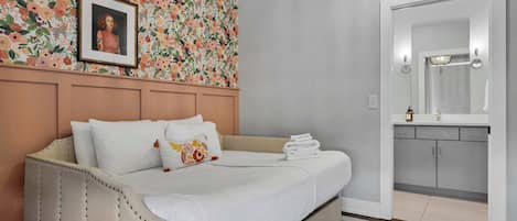 A hotel room with a bed, a floral wallpaper, a framed picture on the wall, and a bathroom visible through an open door.