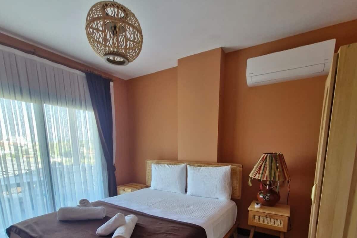 A hotel room with a large bed, a bedside table with a lamp, and a window with curtains.