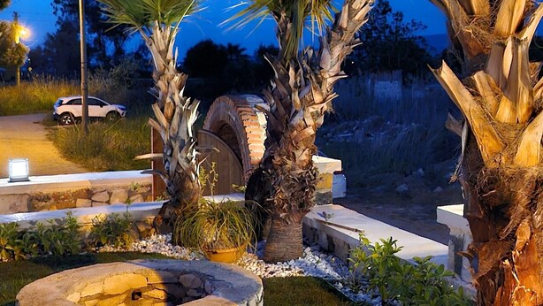Un jardín ajardinado con palmeras, un hogar de piedra y un arco de ladrillo.