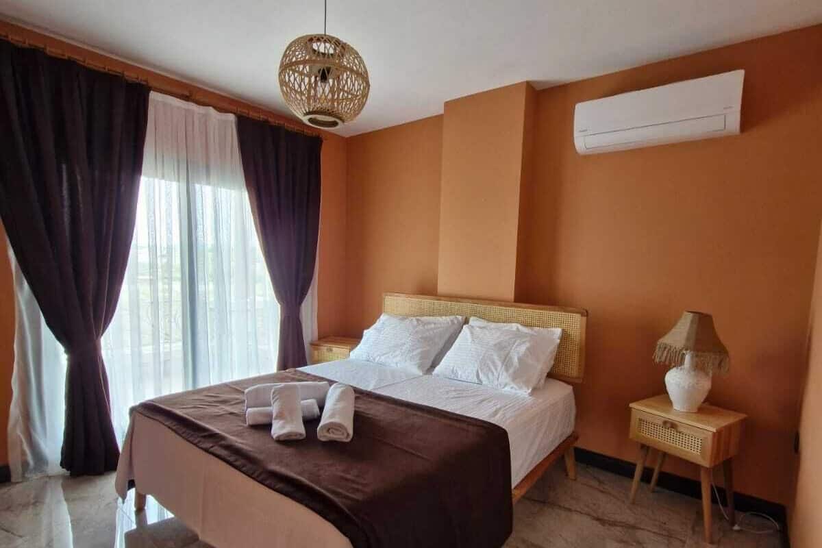 A hotel room with a large bed, a bedside table with a lamp, and an air conditioning unit on the wall.