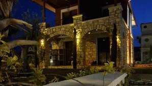 Un edificio de piedra con balcón, rodeado de vegetación e iluminado por luces.