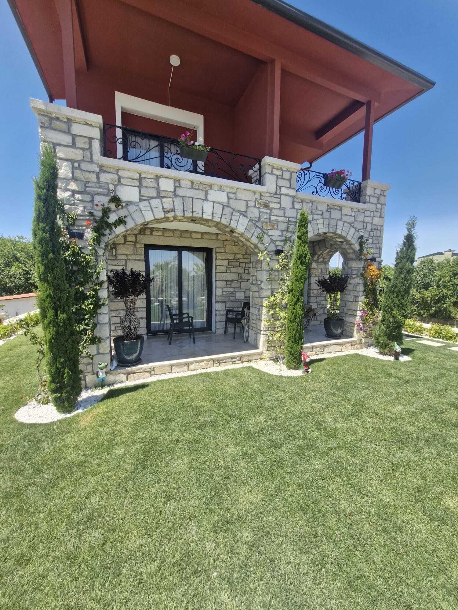 A two-story stone building with a balcony, outdoor seating, and potted plants.
