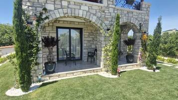 A two-story stone building with a balcony, outdoor seating, and potted plants.