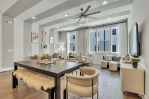 A spacious living room with a dark wooden dining table, multiple seating options, and a ceiling fan.